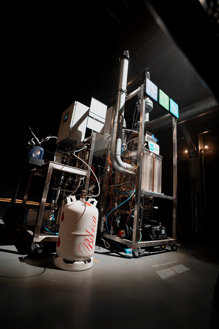 DAC-Laboranlage aus einem Edelstahlrahmen, Rohrleitungen, Messgeräten und Steuerkasten; Leitungsrohre verbinden die Anlage mit einer weißen Gasflasche mit der roten Aufschrift „BIBIZA“